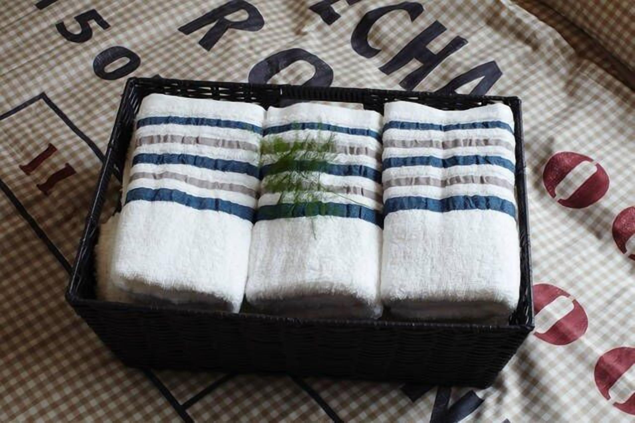 A black woven basket containing four folded white towels with blue stripes.