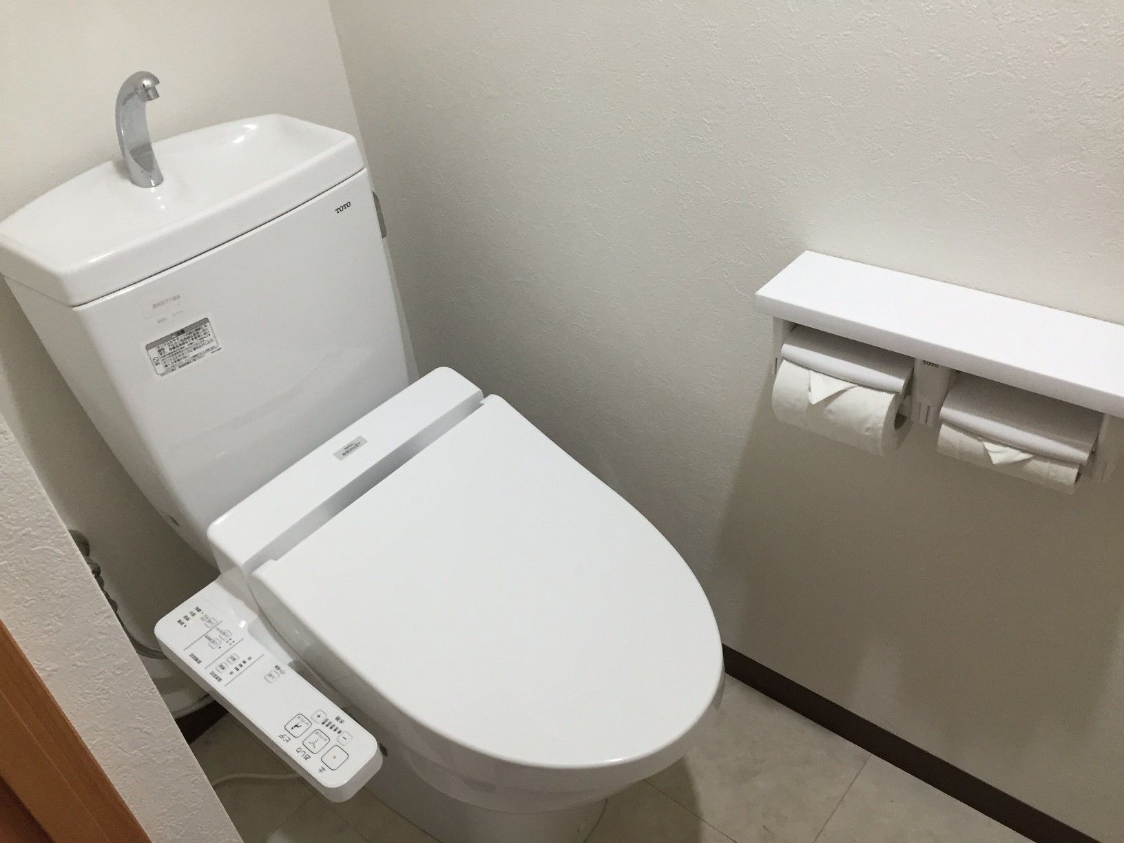 A modern toilet with a control panel, a wall-mounted sink, and a toilet paper holder.