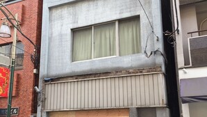 Un edificio de varios pisos con una puerta de garaje, un balcón con baranda metálica y una ventana pequeña con marco de madera.