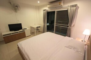 Une chambre d’hôtel avec un lit, un téléviseur posé sur un meuble, un bureau et une fenêtre avec des rideaux.