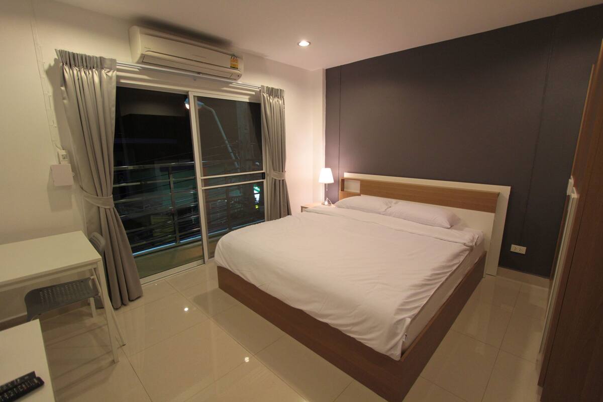 Une chambre d’hôtel équipée d’un lit, d’un bureau, d’une chaise, d’une fenêtre avec des rideaux et d’un appareil de climatisation.