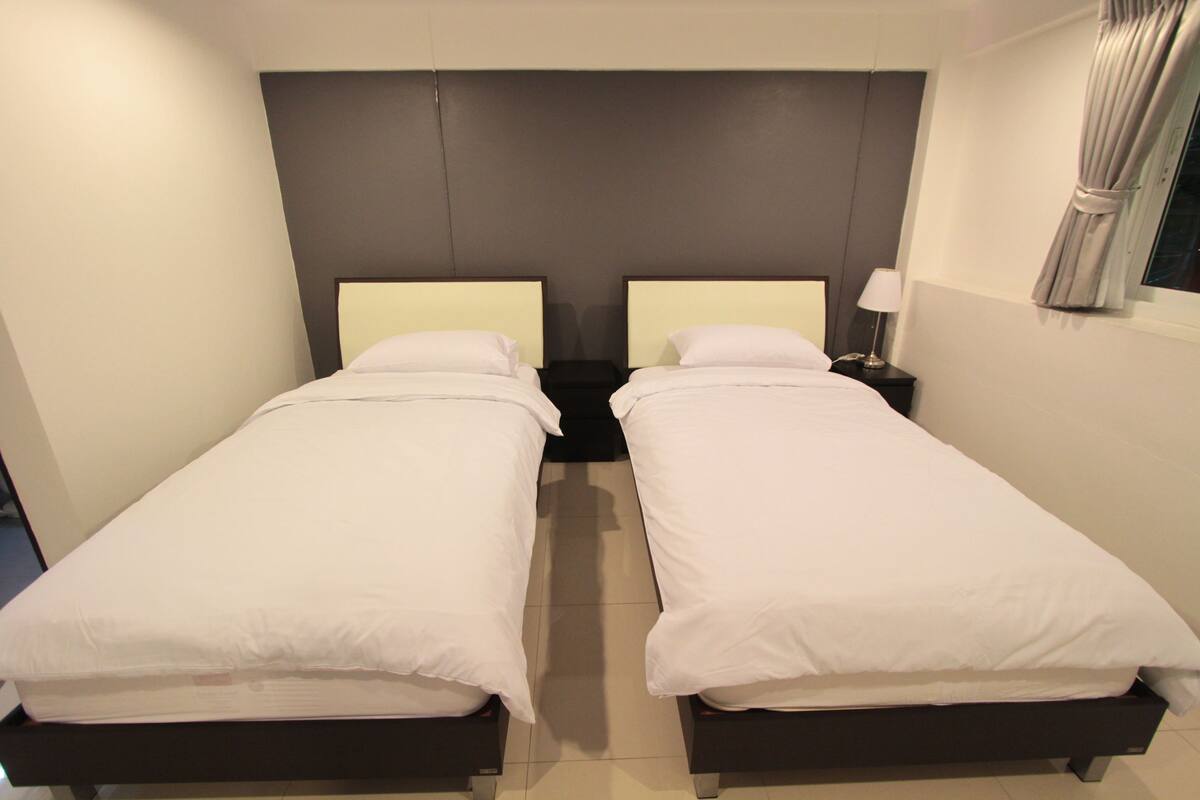 Une chambre double avec deux lits simples, une tête de lit sombre et une table de chevet avec une lampe.