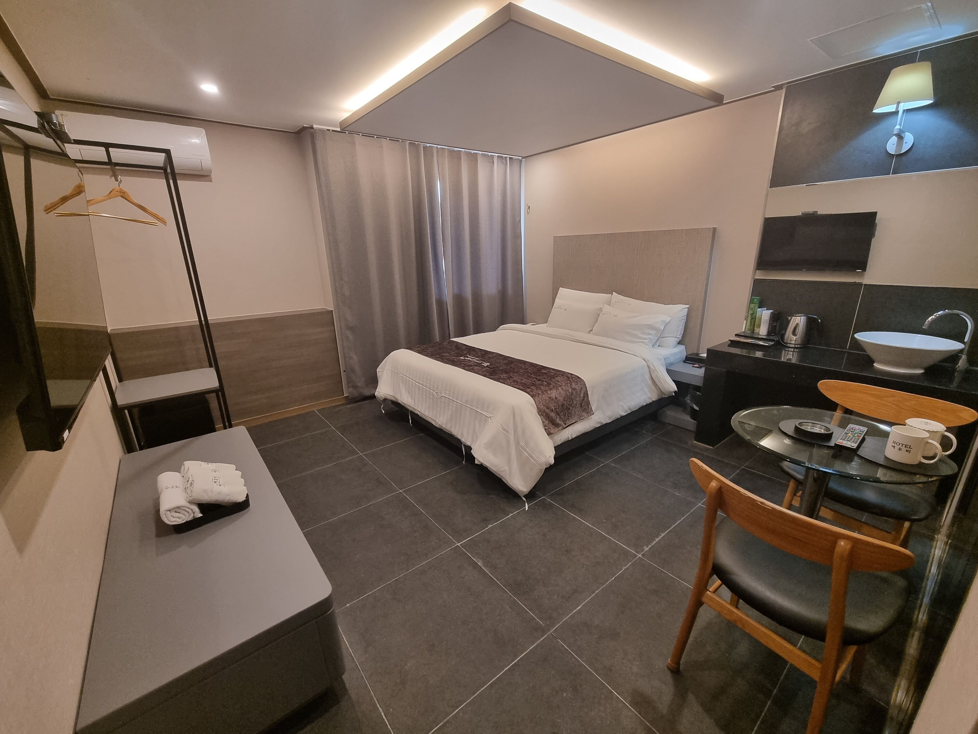 Habitación de hotel con cama, mesita de noche, silla, escritorio y una pequeña mesa con un bol y una taza.