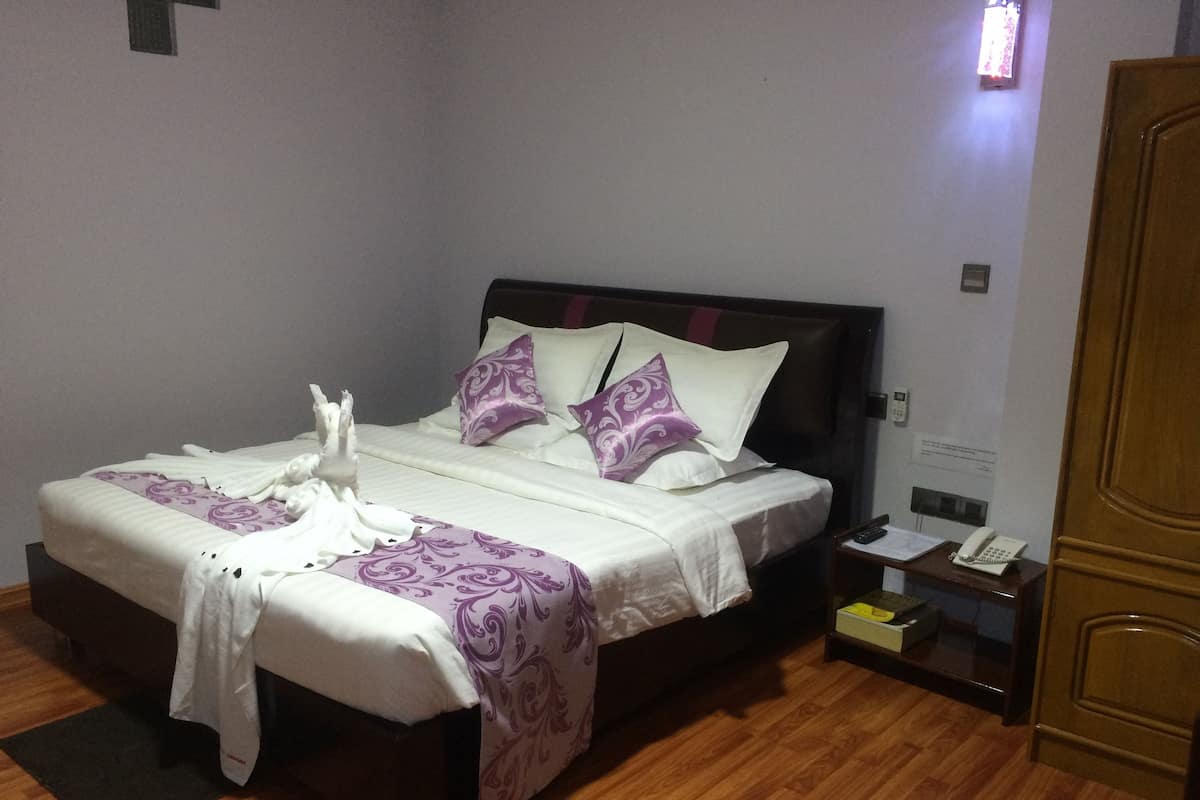 A neatly made bed with white and purple linens, a wooden headboard, and a bedside table with a phone and papers.