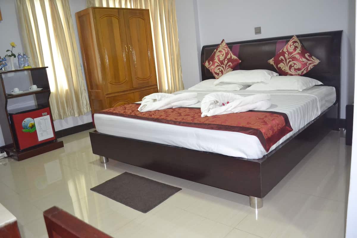 A neatly made bed with white linens and red accents, a wooden wardrobe, and a small desk with a red cabinet.