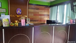 A hotel reception desk with a wooden panel wall, a green accent wall, and a window with blinds. - C & L Suites Inn (Dumaguete)
