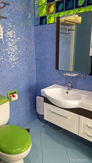 Um banheiro com vaso sanitário verde, pia branca e paredes revestidas de azulejos azuis.