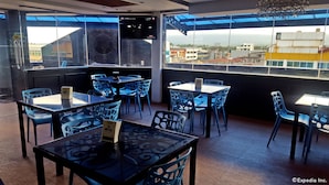 A rooftop restaurant with tables and chairs, large windows offering city views, and a television screen. - C & L Suites Inn (Dumaguete)