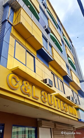 Um hotel com vários andares, varandas, um sinal chamativo de 'C&L Suites Inn' e aparelhos de ar condicionado.