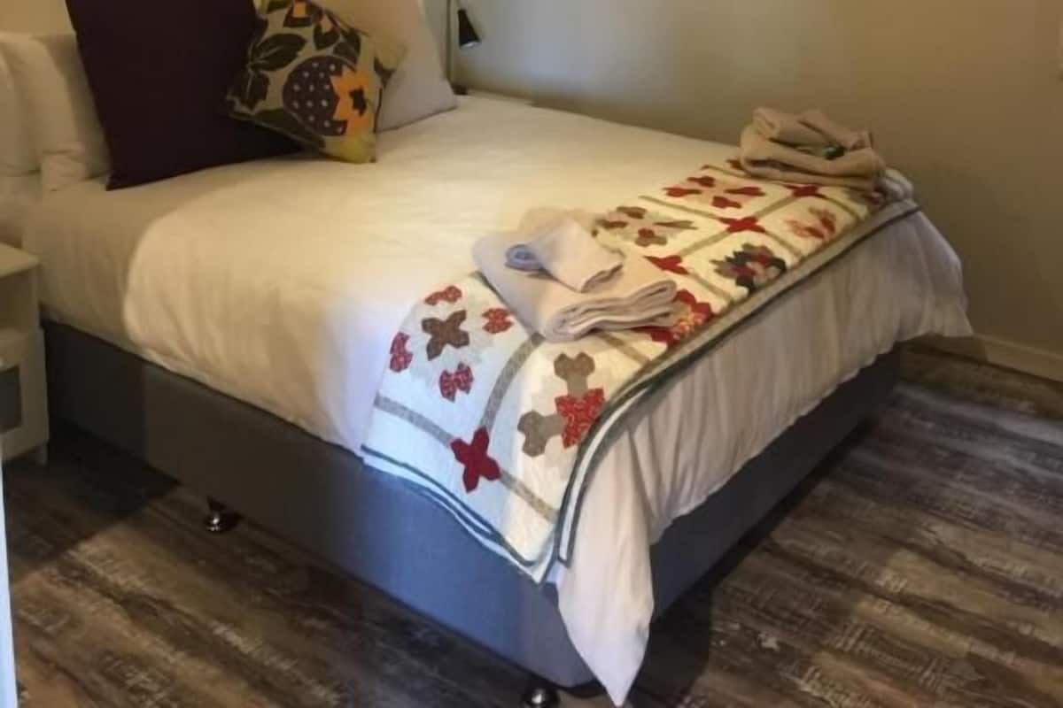 A neatly made bed with a floral-patterned blanket, a bedside table with a lamp, and a wooden floor.