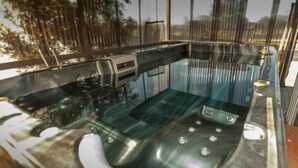 Ein mit Glas umgebenes Whirlbad mit integriertem Sitzplatz und Bedienfeld, umgeben von einem Metallgeländer.