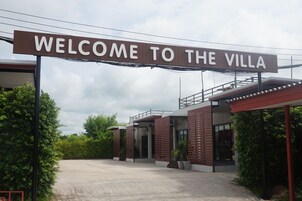 Une entrée moderne pour la villa, avec une pancarte indiquant « BIENVENUE À LA VILLA », une allée couverte et un espace paysager agrémenté de plantes en pot.