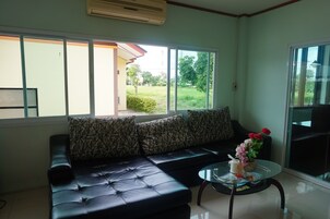 A living room with a black leather sofa, a glass coffee table, and a view of a garden through large windows.