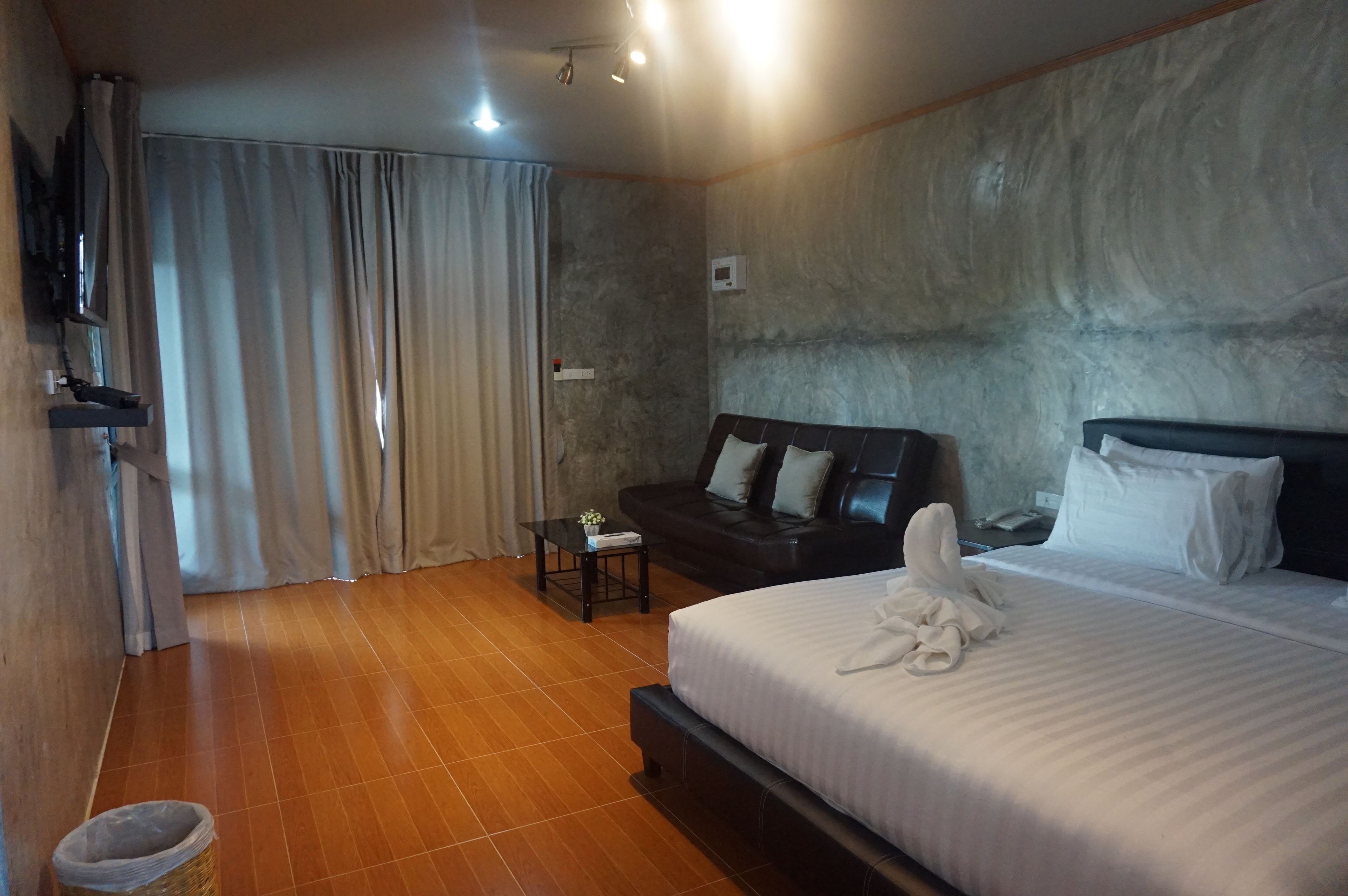 Quarto de hotel com uma cama grande, um sofá, uma pequena mesa com um vaso de flores e uma televisão fixada na parede.