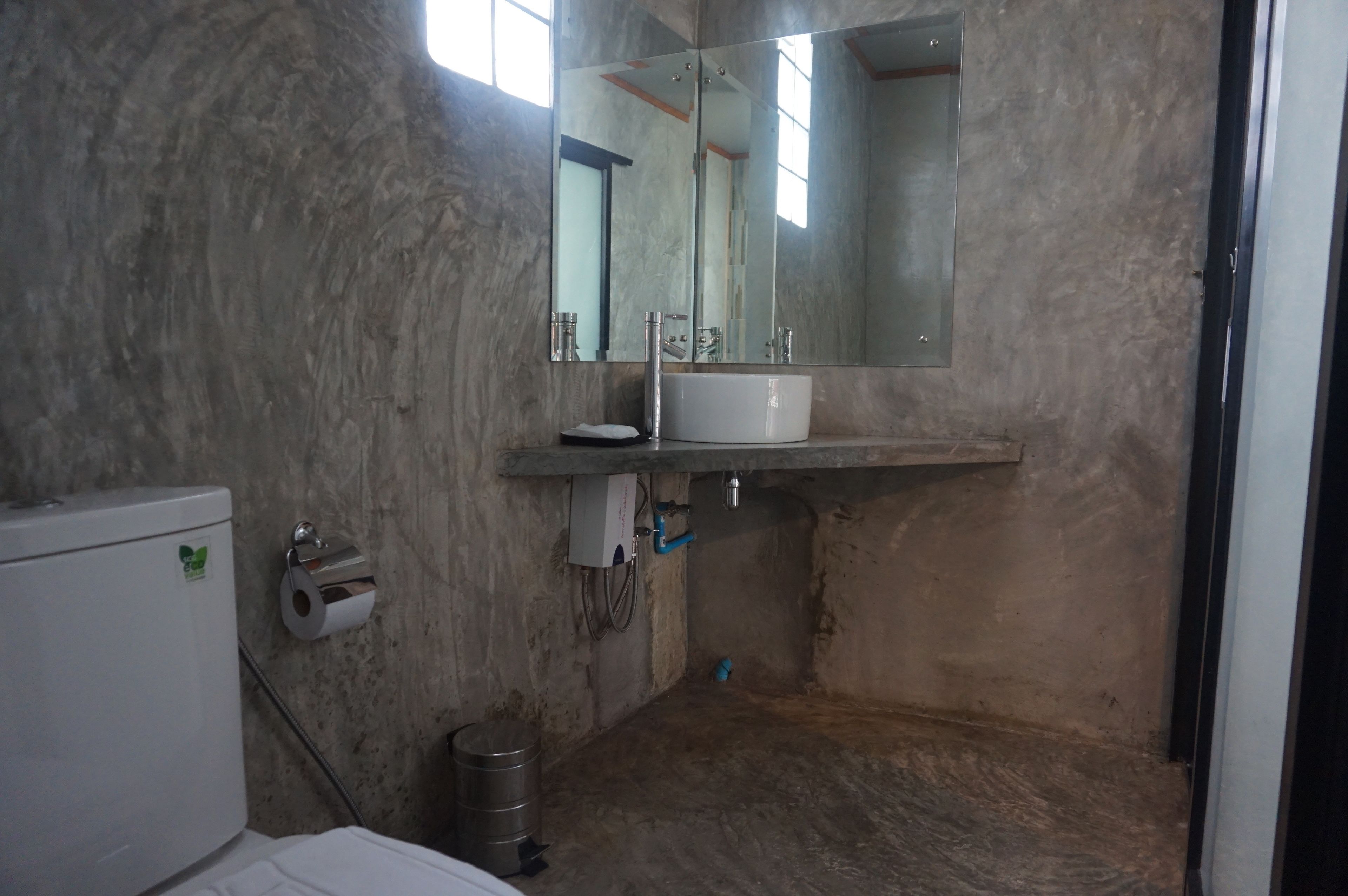 Un baño con pared de mármol, inodoro blanco, lavamanos con espejo y una tubería azul.