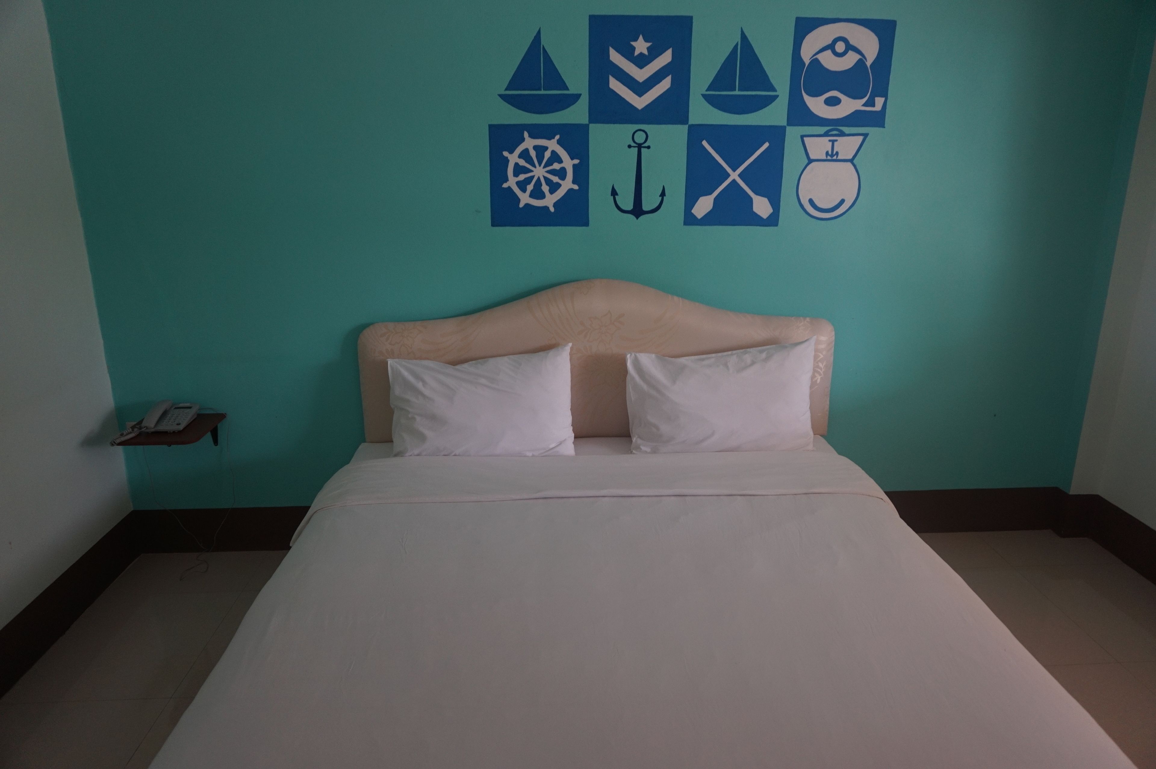 A neatly made bed with white linens in a room with teal walls.