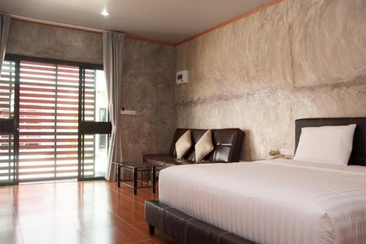 A bedroom with a large bed, a chair, a small table, and a window with blinds.
