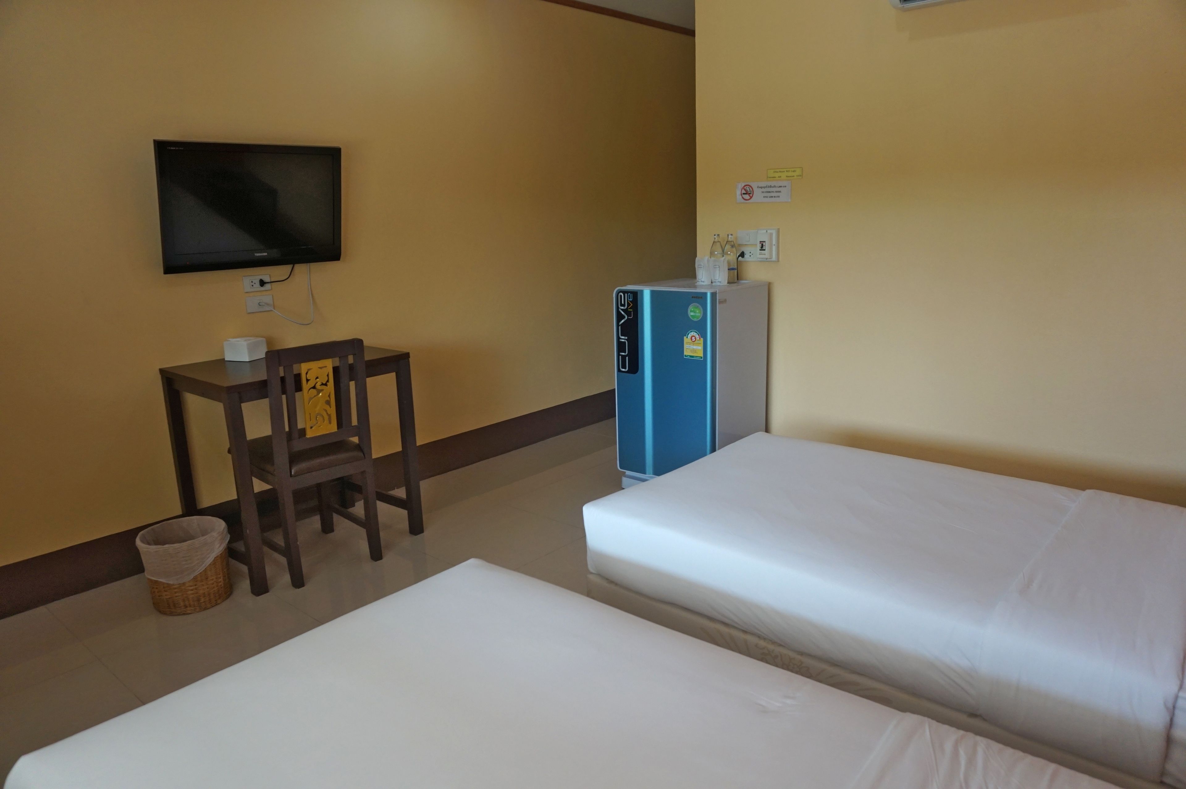 A hotel room with two beds, a desk with a chair, a television, and a minibar.