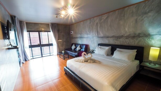 A spacious hotel room with a large bed, a seating area with a sofa and armchairs, a flat-screen TV, and a large window with curtains. - A Nice Resort & Villa (Buriram)