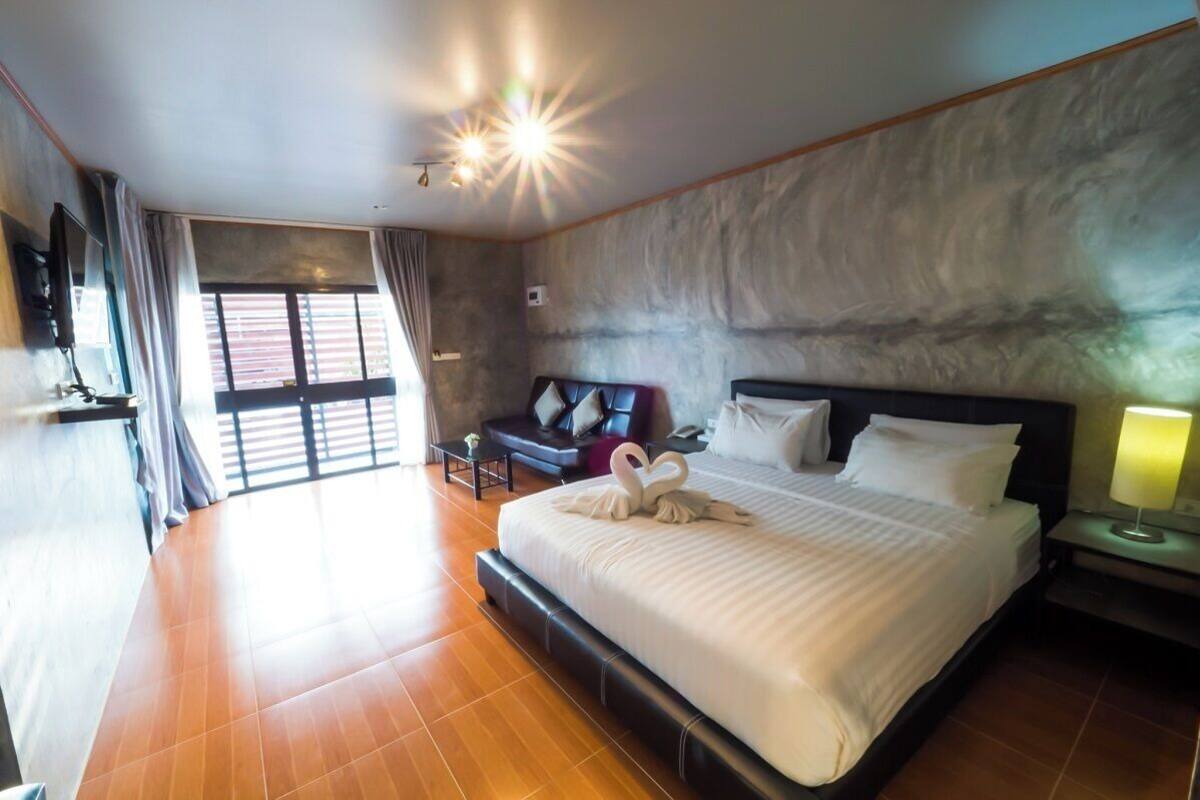 Une chambre d’hôtel spacieuse, dotée d’un grand lit, d’un coin salon avec un canapé et des fauteuils, d’une télévision à écran plat et d’une grande fenêtre avec des rideaux.