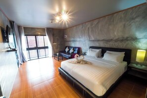 A spacious hotel room with a large bed, a seating area with a sofa and armchairs, a flat-screen TV, and a large window with curtains. - A Nice Resort & Villa (Buriram)