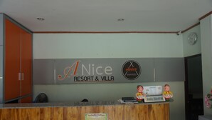 A reception desk with a wooden counter, a clock on the wall, and a sign that reads "A Nice RESORT & VILLA". - A Nice Resort & Villa (Buriram)
