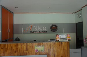 Un comptoir d’accueil avec un plan de travail en bois, une horloge au mur et une enseigne indiquant « A NICE RESORT & VILLA ».