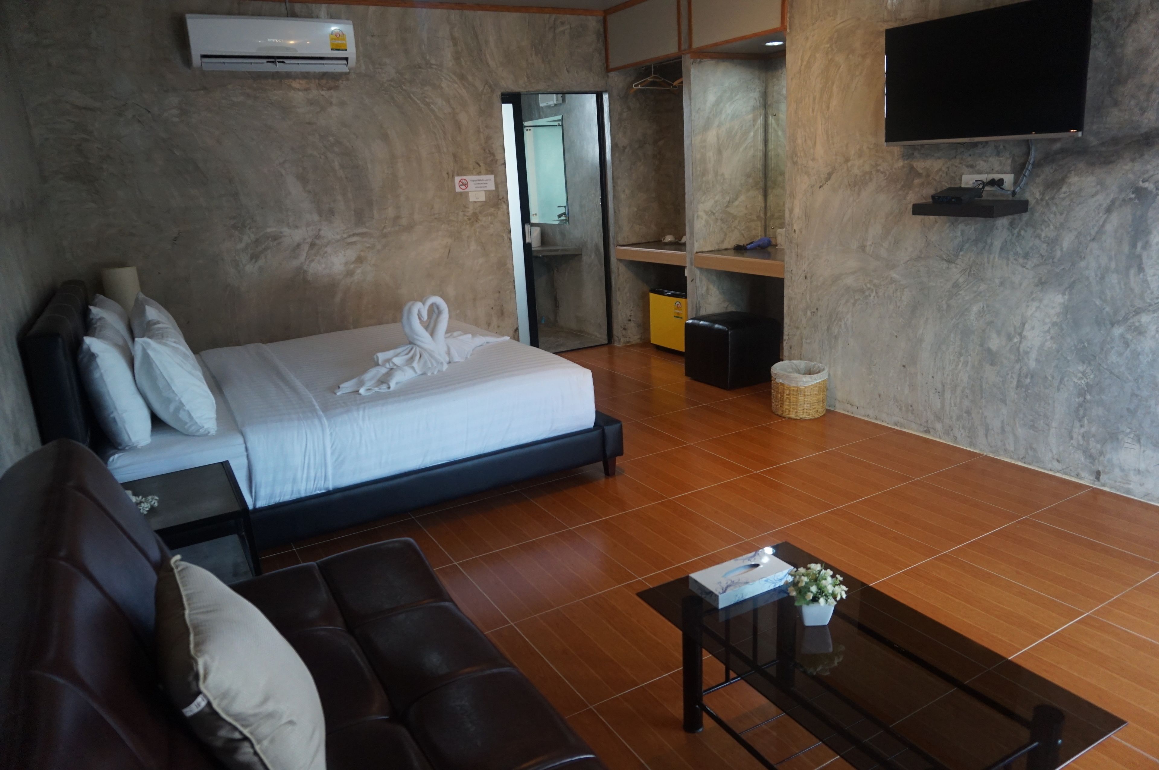 Una habitación de hotel con una cama, un sofá, un televisor y una pequeña mesa con un jarrón.