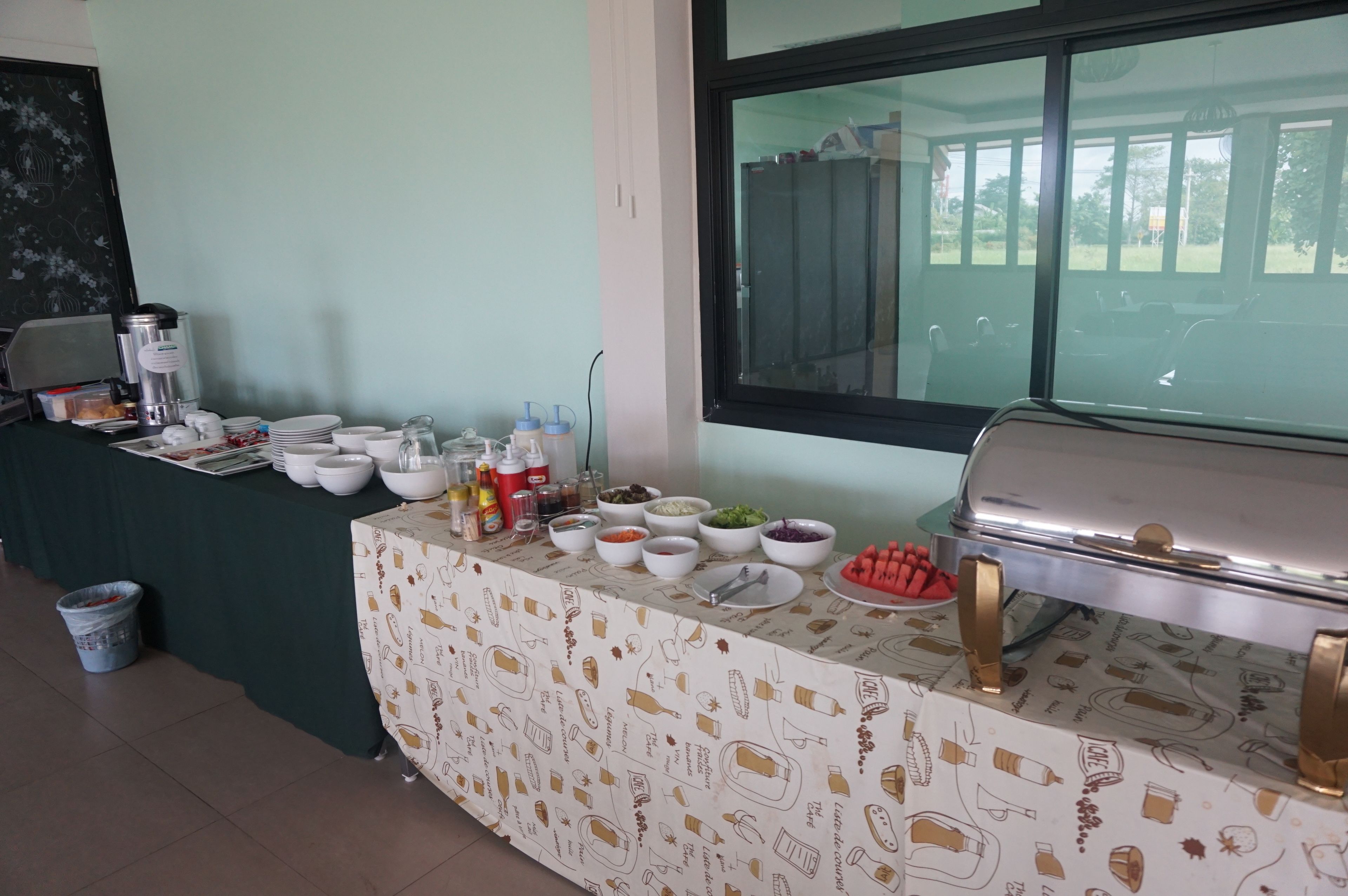 A buffet setup with various food items and condiments, a coffee machine, and a window with a view of the outdoors.