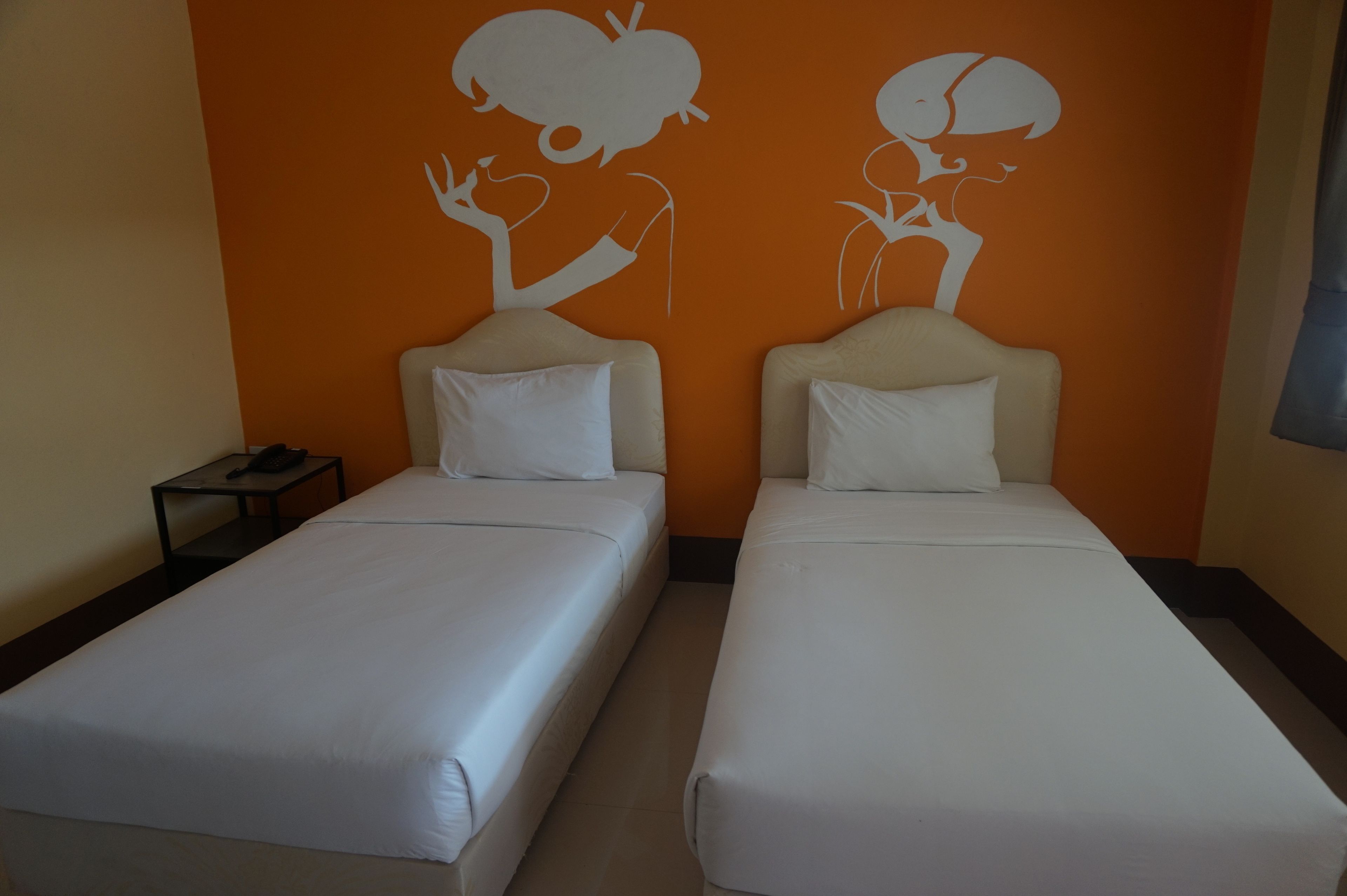 Dos camas individuales con ropa de cama blanca en una habitación con paredes anaranjadas.