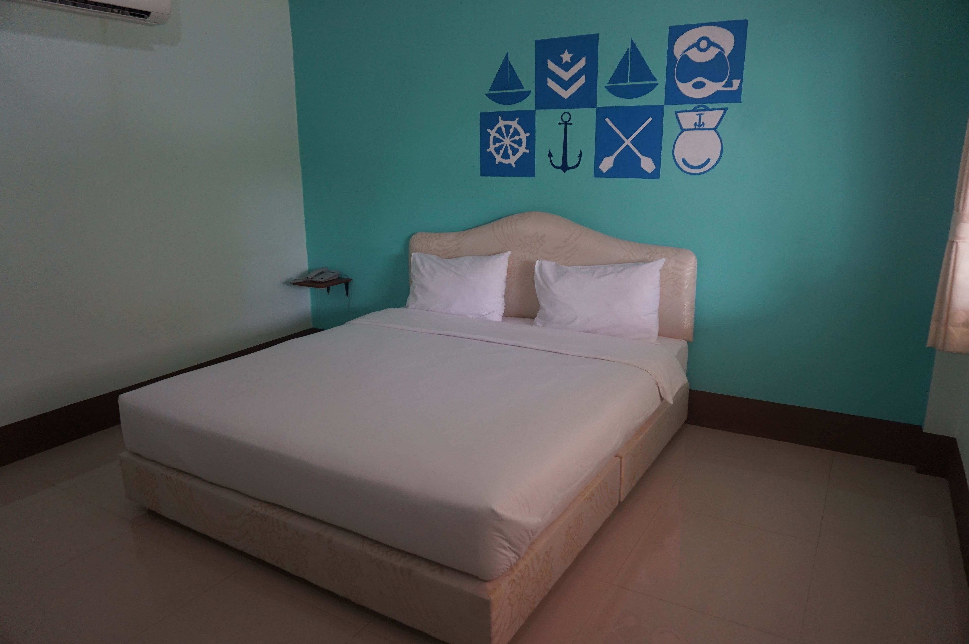 Una cama bien tendida con cabecera, una pared decorada con motivos náuticos y una mesita de noche con lámpara.