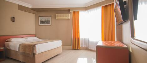 Una habitación de hotel con cama, escritorio, televisión y ventana con cortinas.