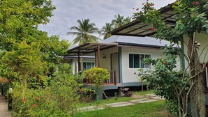 Ein Bungalow mit überdachter Veranda, umgeben von üppiger Vegetation und Palmen.