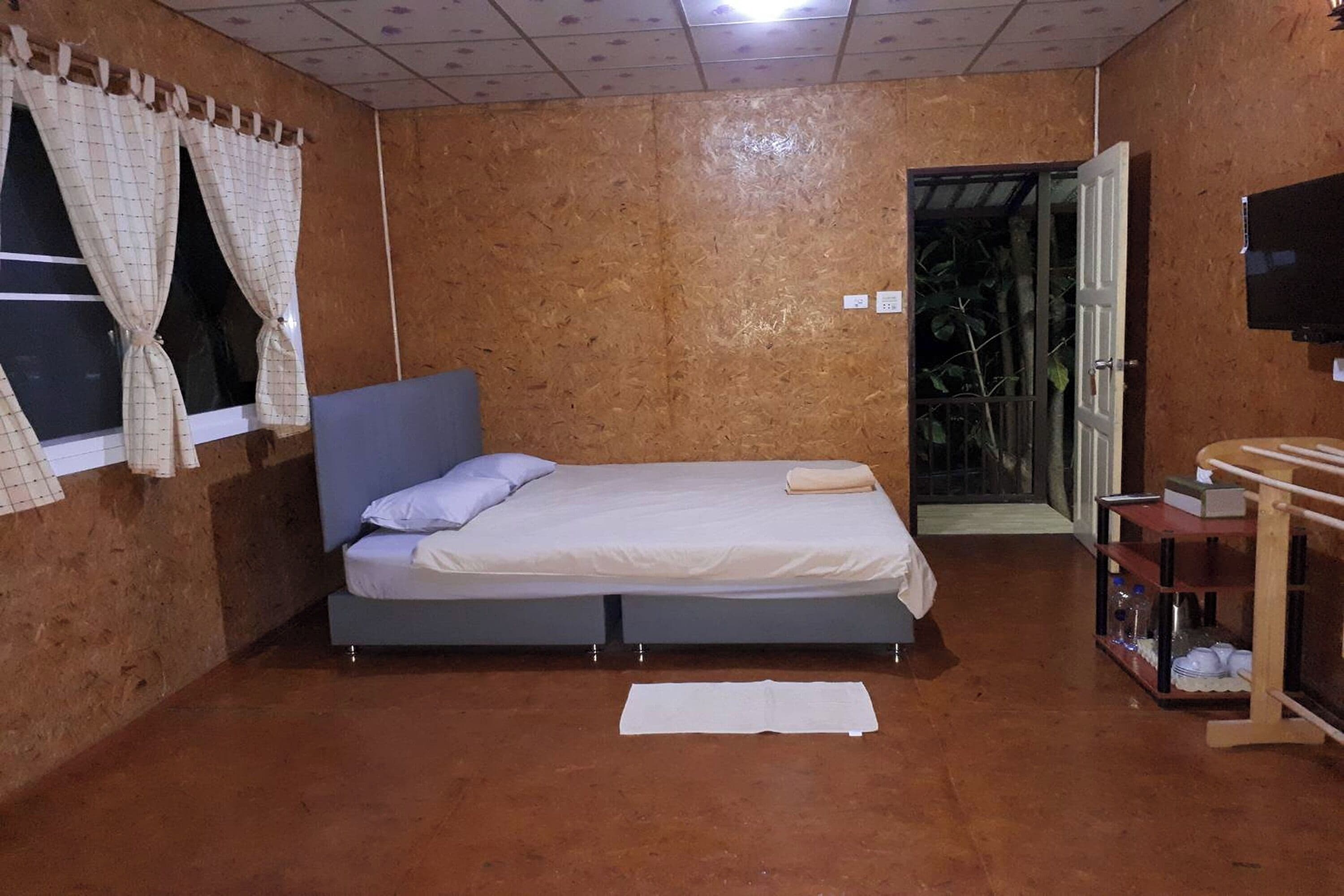 A room with a bed, a small table with a shelf, a TV, and a window with curtains.