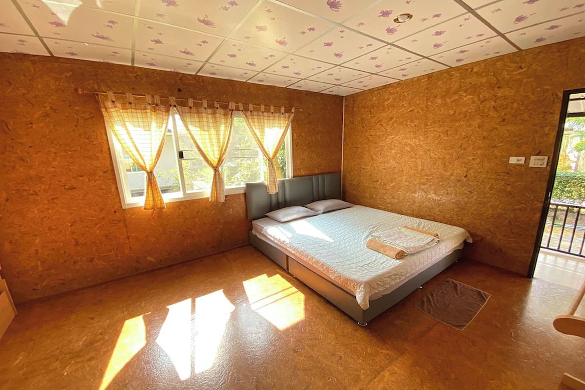 Een kamer met een bed, een raam met gordijnen, een deur en uitzicht op groen.
