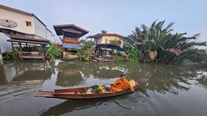Eine Person in einem Boot, umgeben von Wasser und Gebäuden, beladen mit verschiedenen Gegenständen.