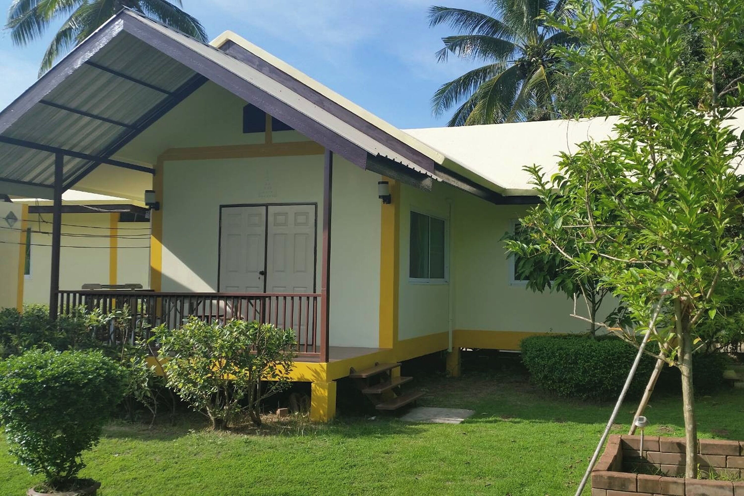 A single-story building with a flat roof, a covered porch, and a small garden area with a tree and shrubs.