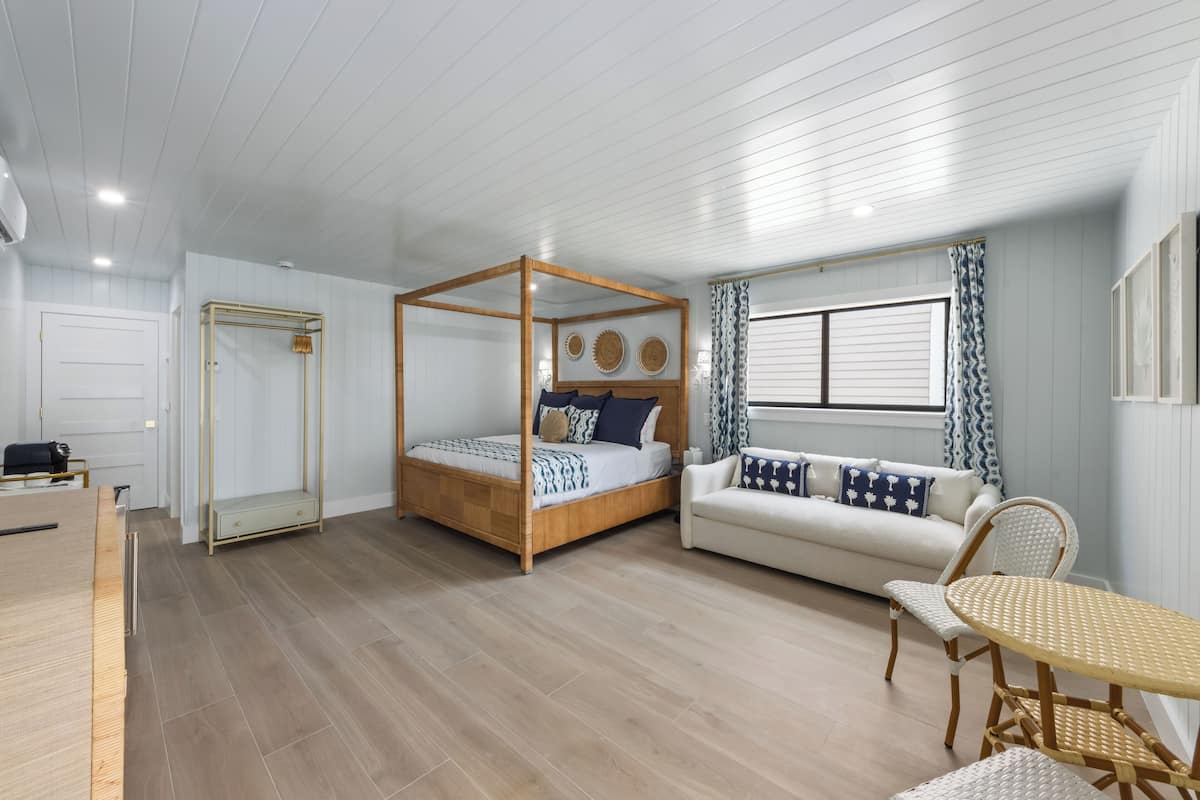 A bedroom with a four-poster bed, a sofa, a dining table, and a mirror.