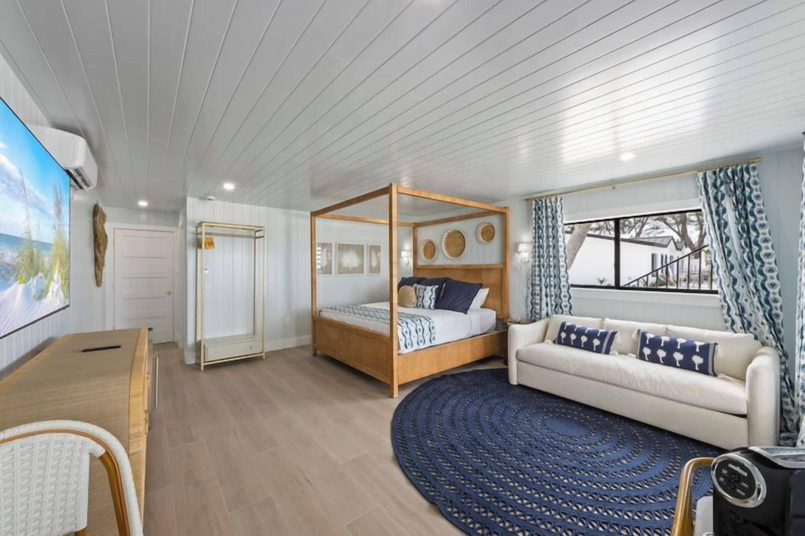Un dormitorio con cama con dosel, un sofá, una alfombra redonda y un televisor.