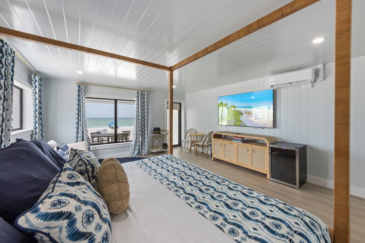 A modern room with a bed, a TV, a desk, and a view of the sea.