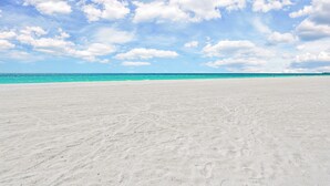 A wide, sandy beach with a clear sky and calm sea.