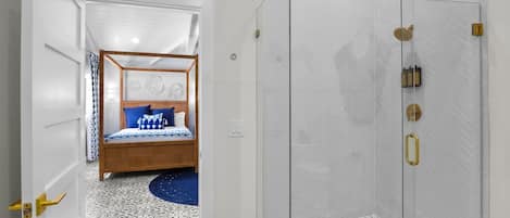 Une salle de bain avec douche, un lit recouvert d’une couvre-lit à motifs bleus et blancs, et un sol à motifs.