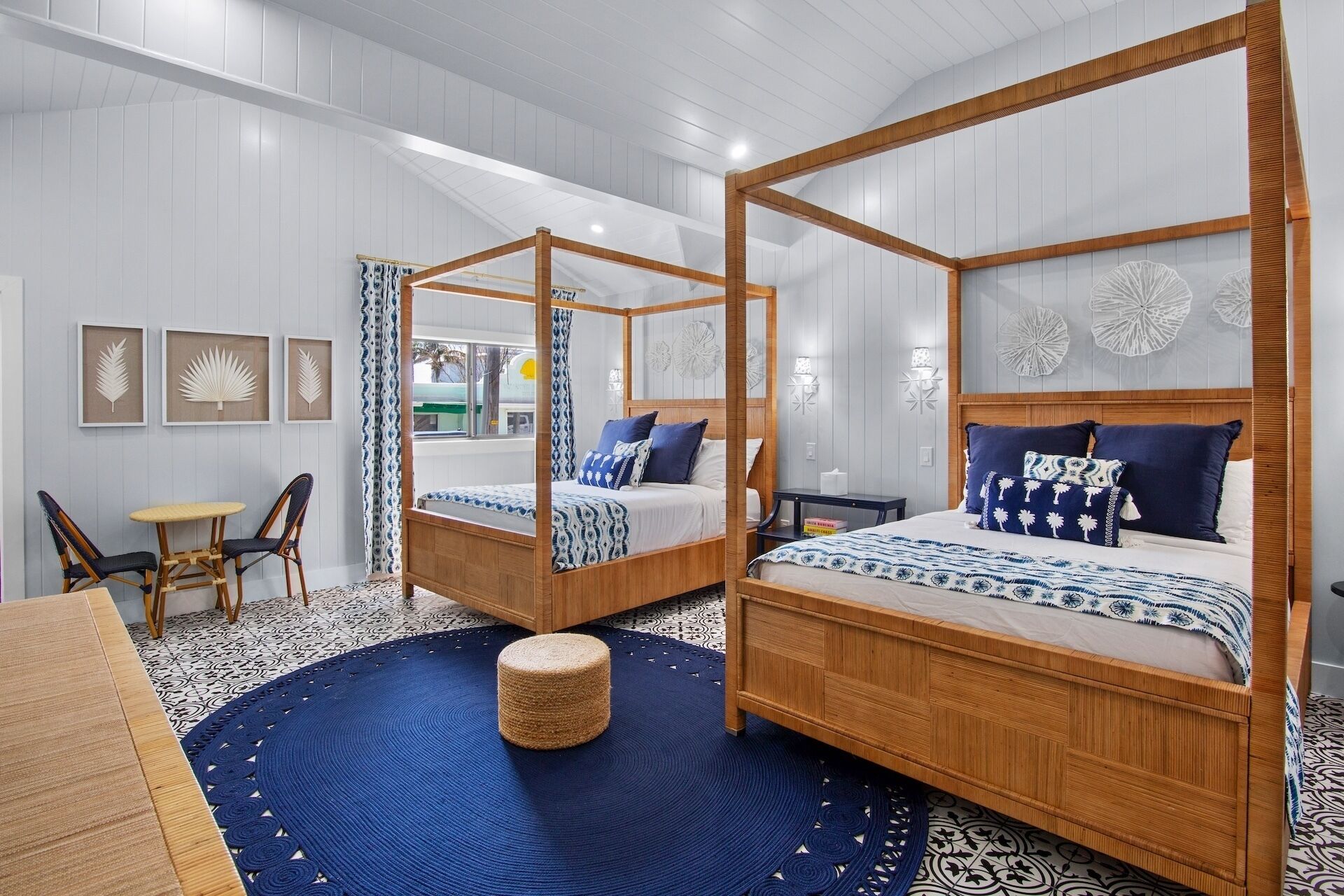 Ein Zimmer mit zwei Himmelbetten, einem runden gewebten Hocker, einem Esstisch mit Stühlen und Blick ins Freie.