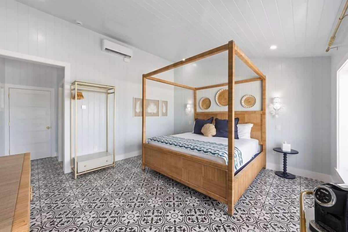 A bedroom with a four-poster bed, patterned floor, and a small table with a candle.