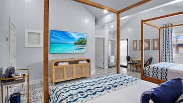 Quarto de hotel moderno com uma cama grande, televisão fixada na parede, um armário de madeira e um banheiro visível através de uma porta aberta.