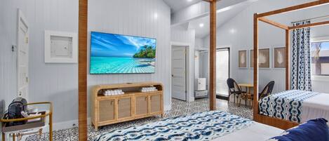 A modern hotel room with a large bed, a TV mounted on the wall, a wooden cabinet, and a bathroom visible through an open door.