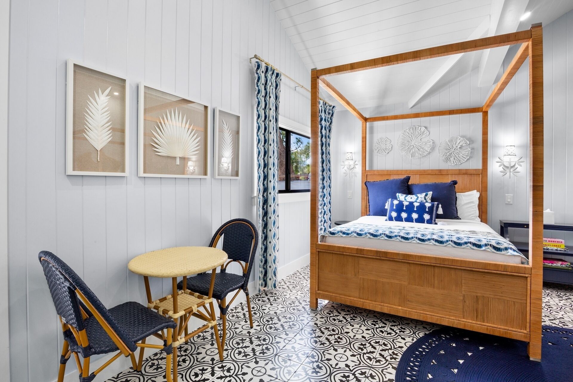 A four-poster bed with a wooden frame, a small round table with chairs, and wall-mounted artwork.