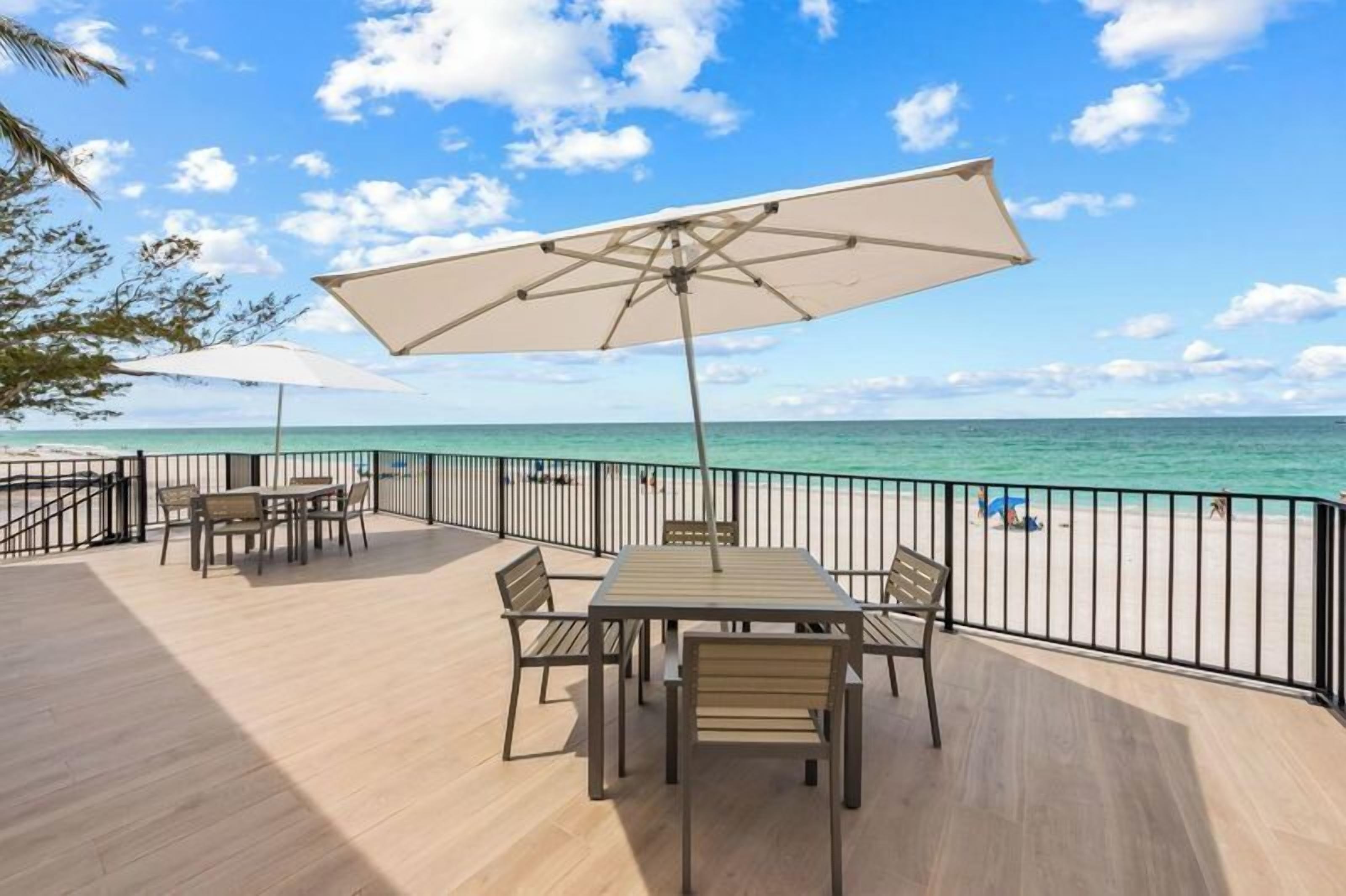 Une terrasse avec une table et des chaises, donnant sur une plage sous un ciel dégagé.