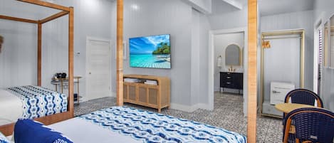 A hotel room with a large bed, a TV, a wooden wardrobe, a bathroom with a mirror, and a chair.