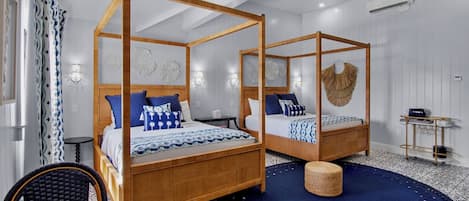 A four-poster bed with a wooden frame, a round woven stool, and a patterned rug.